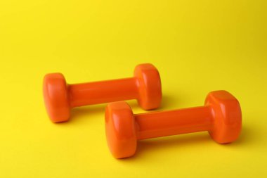 Two stylish orange dumbbells on yellow background