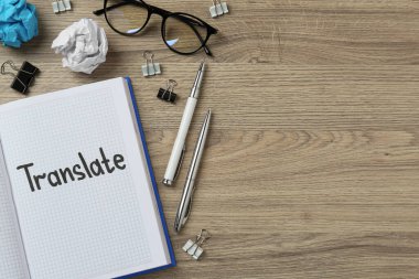 Flat lay composition with word Translate written in notebook on wooden table. Space for text