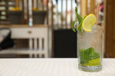 Glass of refreshing citrus drink on white table in cafe, space for text