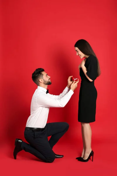 Man with engagement ring making marriage proposal to girlfriend on red background