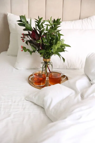 Tray with cups of tea and floral decor near soft blanket on bed