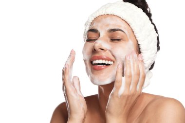 Beautiful woman applying facial cleansing foam on white background