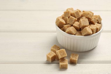Brown sugar cubes on white wooden table, space for text