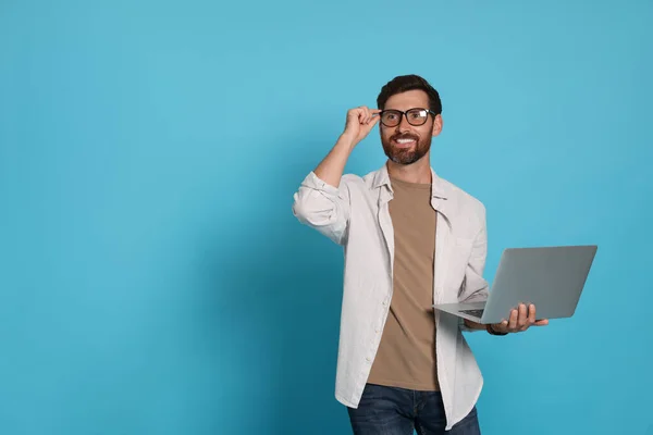 Handsome man with laptop on light blue background