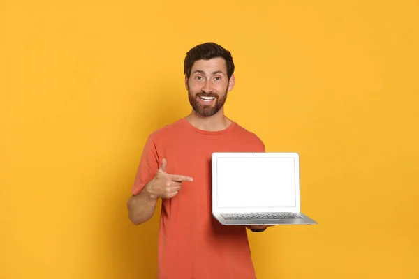 Handsome man with laptop on orange background