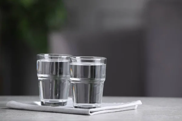 Glasses of clean water on light grey table indoors, space for text