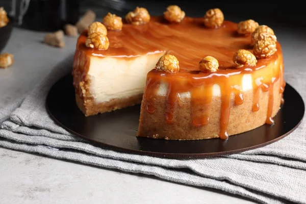 Sliced delicious cheesecake with caramel and popcorn on light grey table, closeup