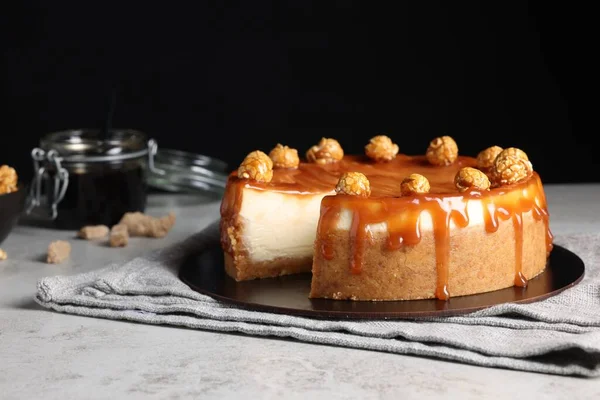Sliced delicious cheesecake with caramel and popcorn on light grey table, space for text