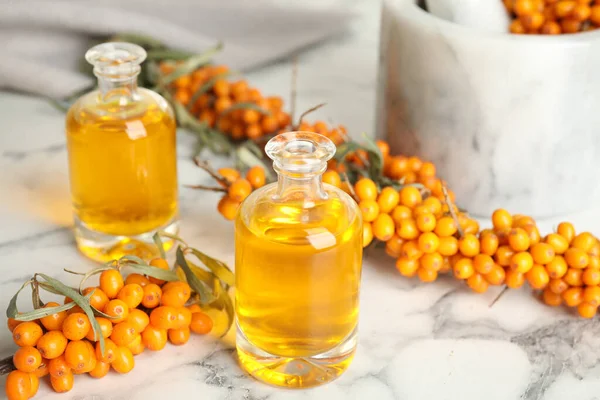 Natural sea buckthorn oil and fresh berries on white marble table