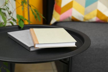 Books on black table near sofa indoors, closeup