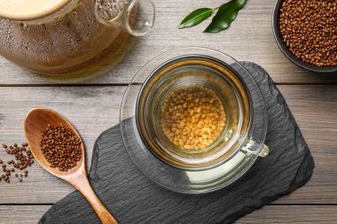 Cup of freshly made aromatic buckwheat tea and granules on wooden table, flat lay