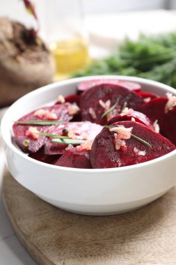 Bowl with raw beetroot slices, garlic and rosemary on wooden board, closeup