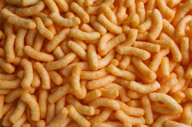 Many crunchy cheesy corn puffs as background, top view