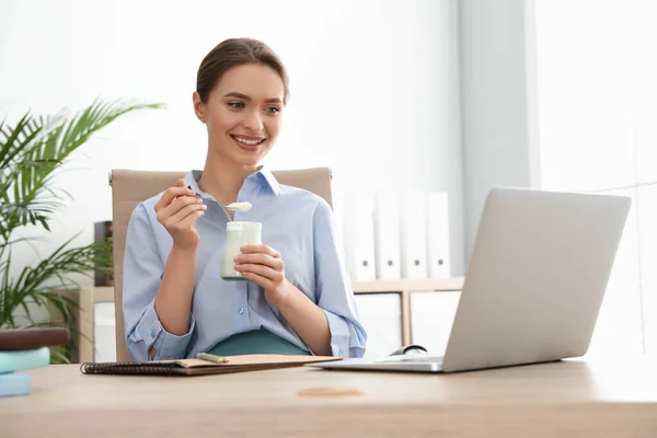 Young attractive woman with tasty yogurt at table in office