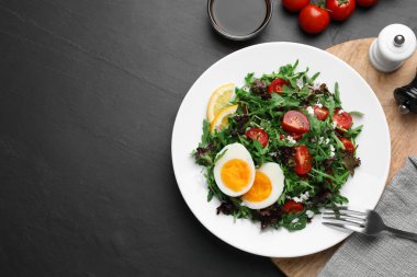 Delicious salad with boiled egg, arugula and tomatoes served on black table, flat lay. Space for text
