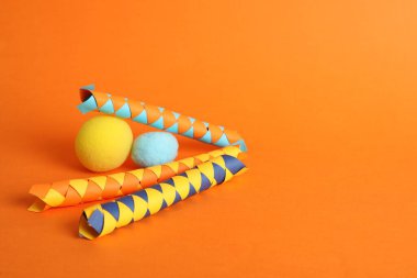Chinese finger traps and clown noses on orange background, space for text