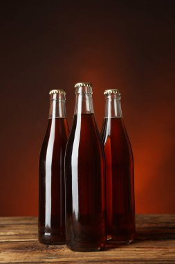 Bottles of delicious kvass on wooden table against brown background
