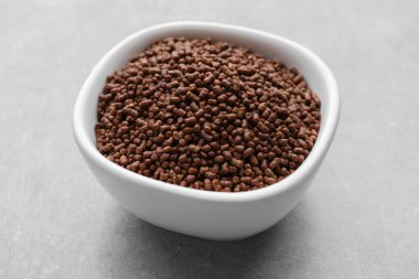 Buckwheat tea granules in bowl on light grey table, closeup