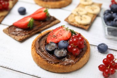Fresh rye crispbreads and rusks with different toppings on white wooden table, closeup