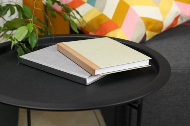 Books on black table near sofa indoors, closeup
