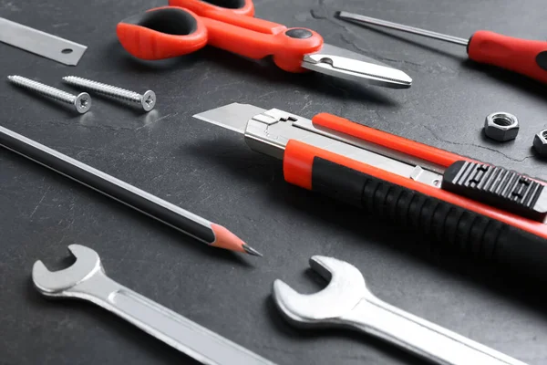 Utility knife and different tools on black table, closeup