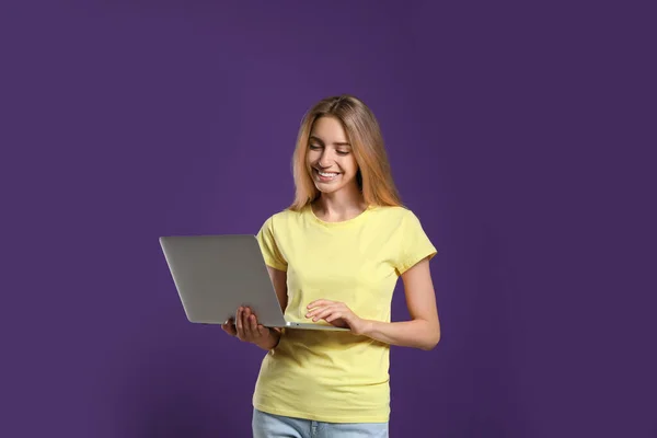 Portrait of young woman with modern laptop on purple background