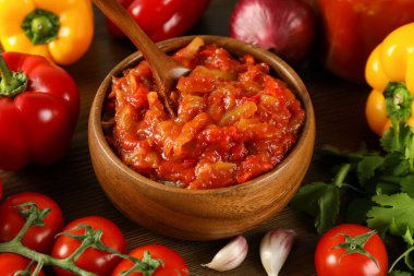 Tasty lecho in wooden bowl and fresh ingredients on table, closeup