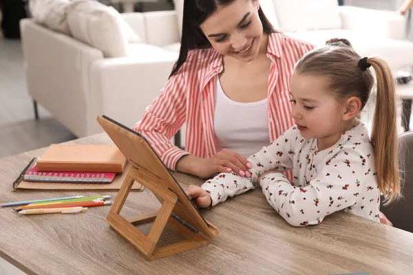 Mother helping her daughter with homework using tablet at home