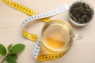 Composition with glass cup of diet herbal tea and measuring tape on wooden background, flat lay