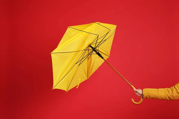 Woman holding umbrella caught in gust of wind on red background, closeup