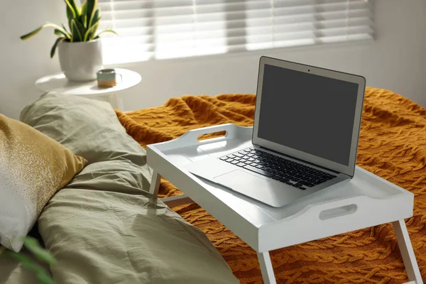 White tray with modern laptop on bed indoors
