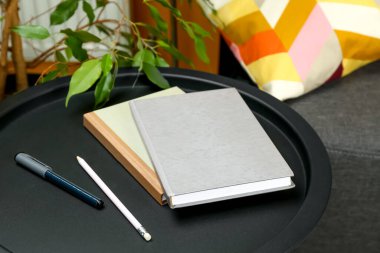 Books, pen and pencil on black table near sofa indoors, closeup