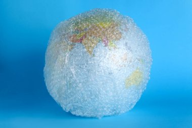 Globe packed in bubble wrap on turquoise background. Environmental conservation