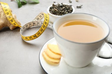 Cup of herbal diet tea and measuring tape on light table, closeup