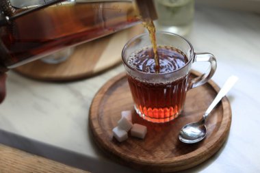 Pouring delicious tea into glass cup on table, closeup