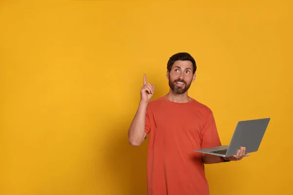 Handsome man with laptop on orange background