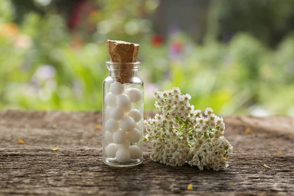 Bottle of homeopathic remedy and beautiful flowers on wooden table