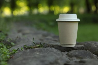 Cardboard takeaway coffee cup with lid on stones outdoors, space for text
