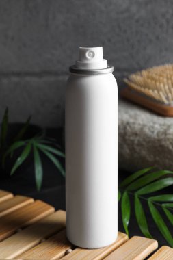 Dry shampoo spray, hairbrush and towel on wooden table near grey wall