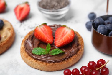 Tasty organic rusk with chocolate spread, strawberry and mint on white marble table, closeup