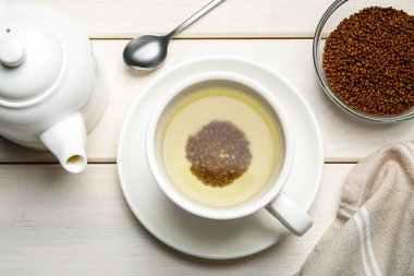 Bir fincan karabuğday çayı, granüller ve çaydanlık beyaz ahşap masada, düz yerde.