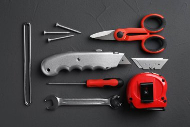 Utility knife with blades among other tools on dark grey background, flat lay