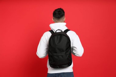 Young man with stylish backpack on red background, back view