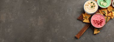 Different delicious hummuses and tortilla chips on grey table, top view with space for text. Banner design