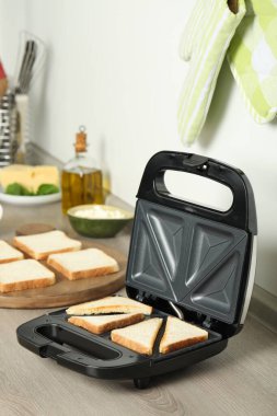 Modern sandwich maker with bread slices on wooden table