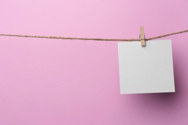 Wooden clothespin with blank notepaper on twine against pink background. Space for text