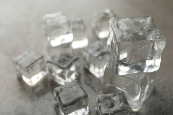 Crystal clear ice cubes with water drops on grey table, closeup