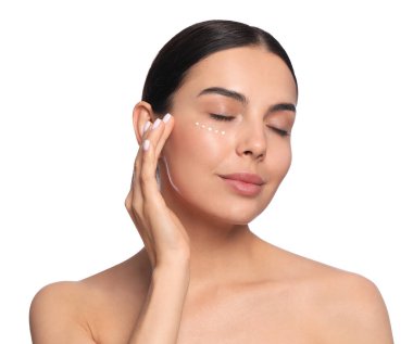 Beautiful young woman with cream on skin under eye against white background