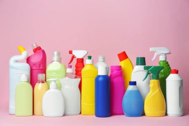 Many bottles of different detergents on pink background. Cleaning supplies