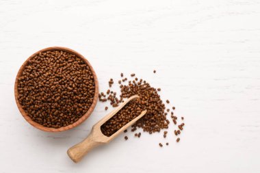 Scoop and bowl with buckwheat tea granules on white wooden table, flat lay
